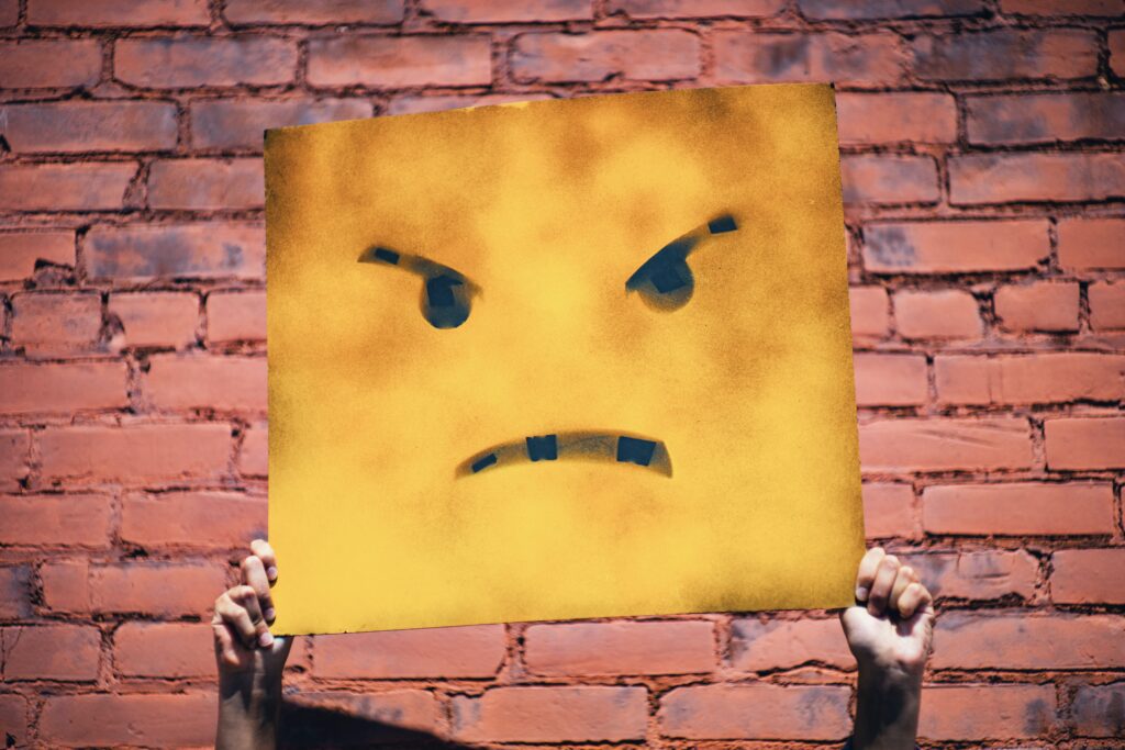 A person holding up a yellow sign with an angry face on it.